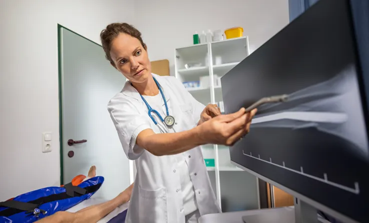 A doctor in a white coat compares a metal medical implant with an X-ray image of a foot on a screen (photo)